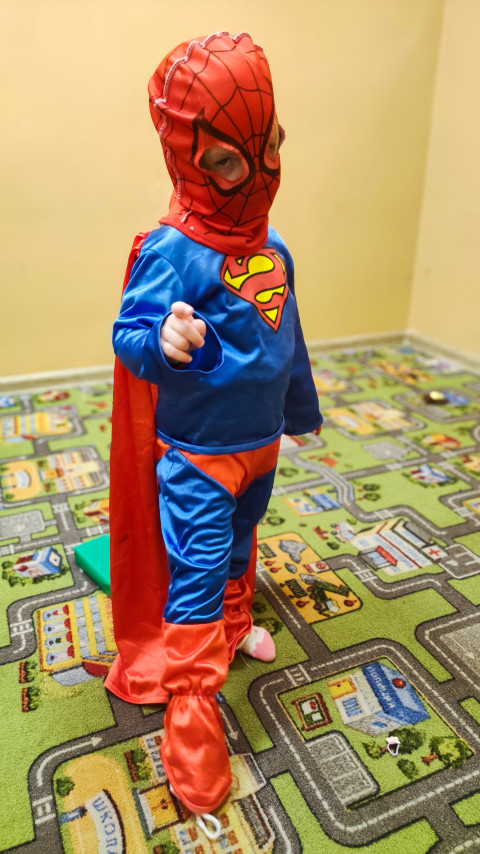 Ребенок в костюме Супермена и маске Человека-паука в игровой комнате