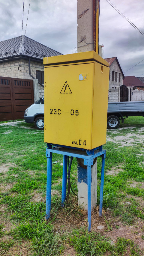 Жёлтый электрический шкаф на опоре у частных домов