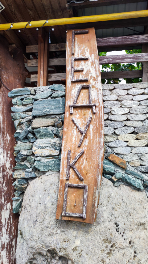 Вертикальная деревянная вывеска «Гедуко» из веток на каменной стене