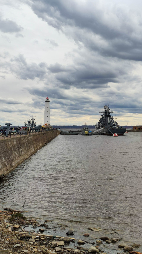 Маяк в Кронштадте на фоне военных кораблей и облачного неба
