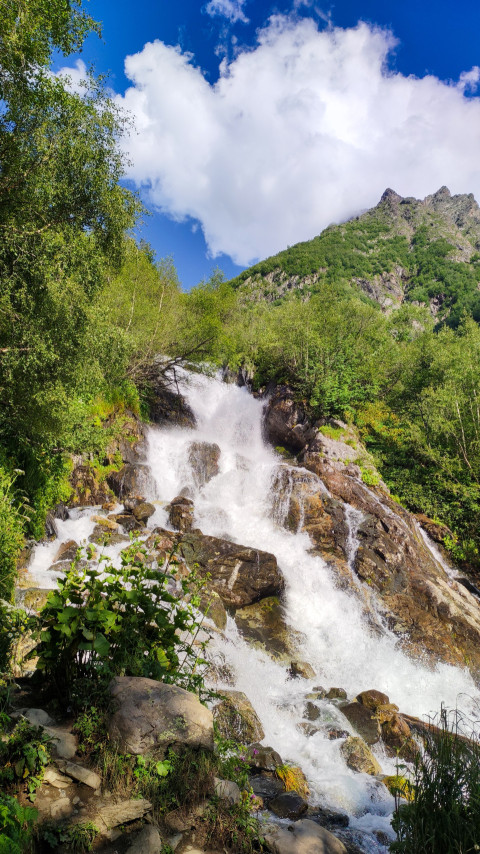 Водопад на фоне гор с зеленью и облаками в ясный день