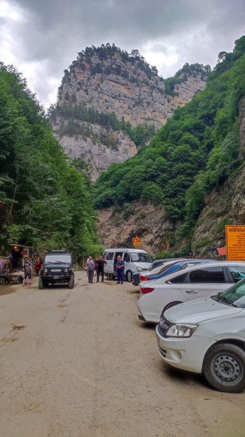 Парковка с несколькими автомобилями и людьми на фоне гор в Чегемском ущелье