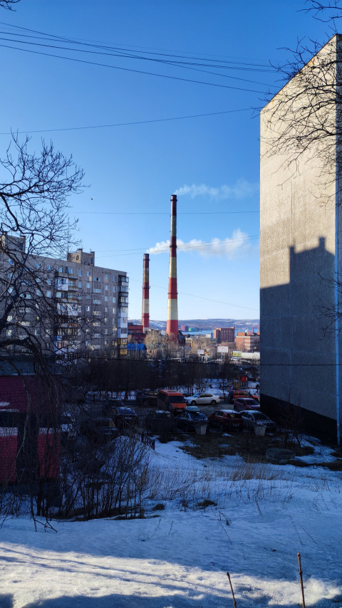 Вид на жилые дома и дымящиеся трубы на фоне голубого неба в городском районе