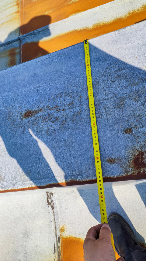 Замер металлической кровли с помощью рулетки на крыше здания