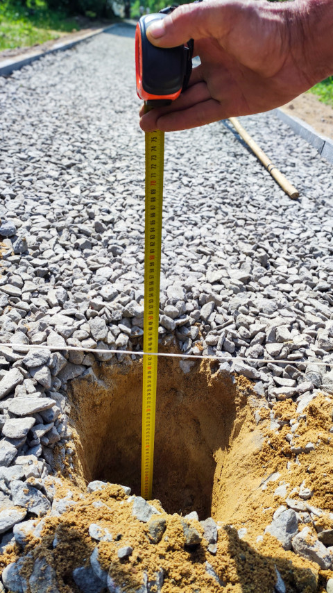 Рулетка опущена в яму для замера глубины на гравийной дорожке