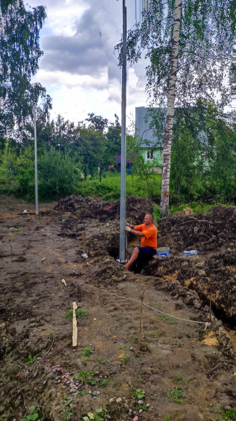 Рабочий устанавливает металлическую опору в грунт