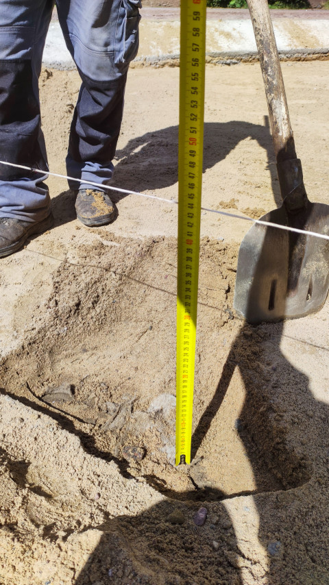 Измерение глубины ямы строительной рулеткой на песчаном основании