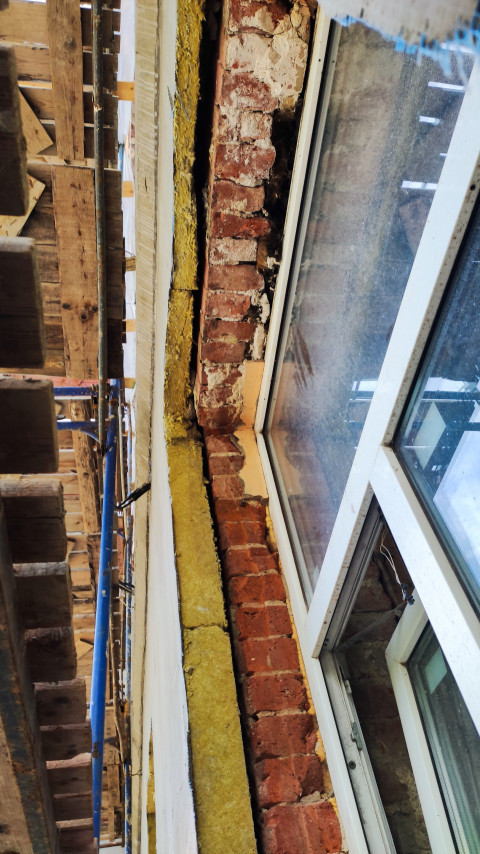 Фрагмент кирпичной стены с утеплителем и окном в процессе ремонта