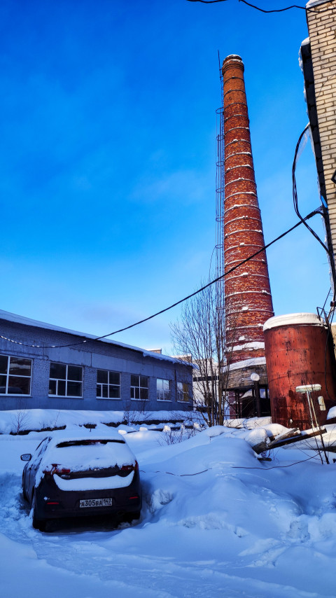 Кирпичная дымовая труба и заснеженная территория промышленного двора