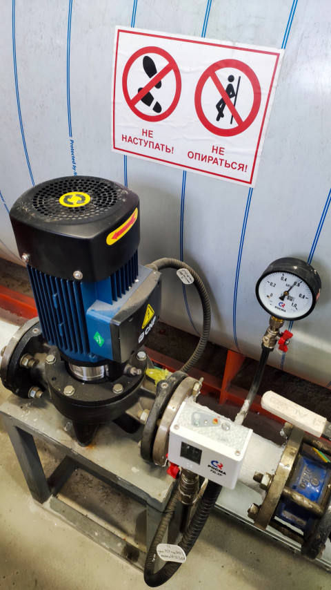 Знак безопасности на фоне насосного узла и манометра