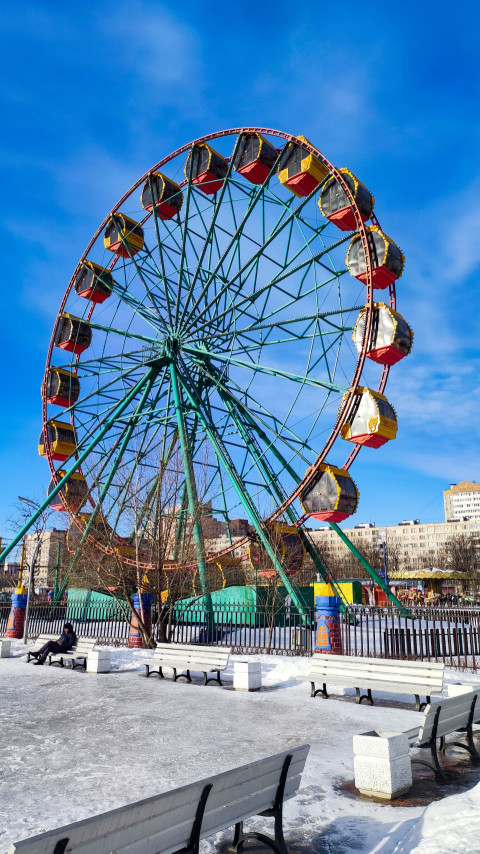 Колесо обозрения в зимнем парке и скамейки на переднем плане