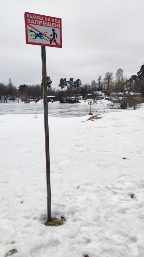 Предупреждающий знак на деревянной опоре у замерзшего водоёма