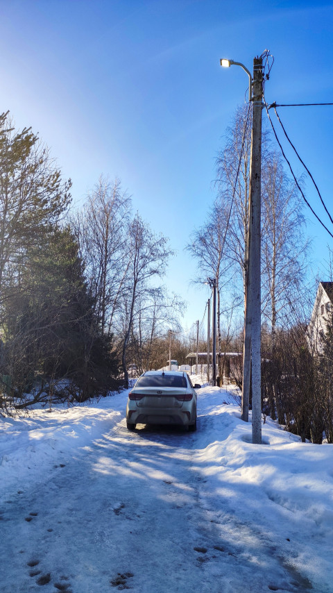 Легковой автомобиль, припаркованный у заснеженной улицы с линиями электропередачи