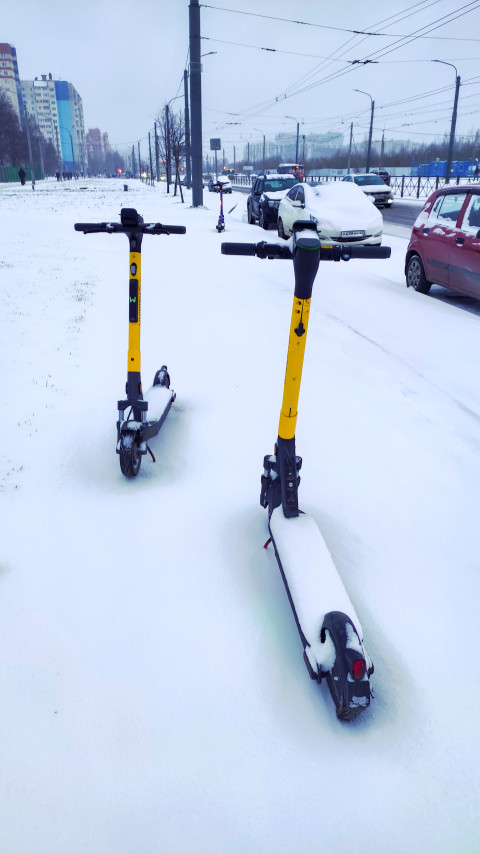 Электросамокаты на снегу у городской дороги зимой