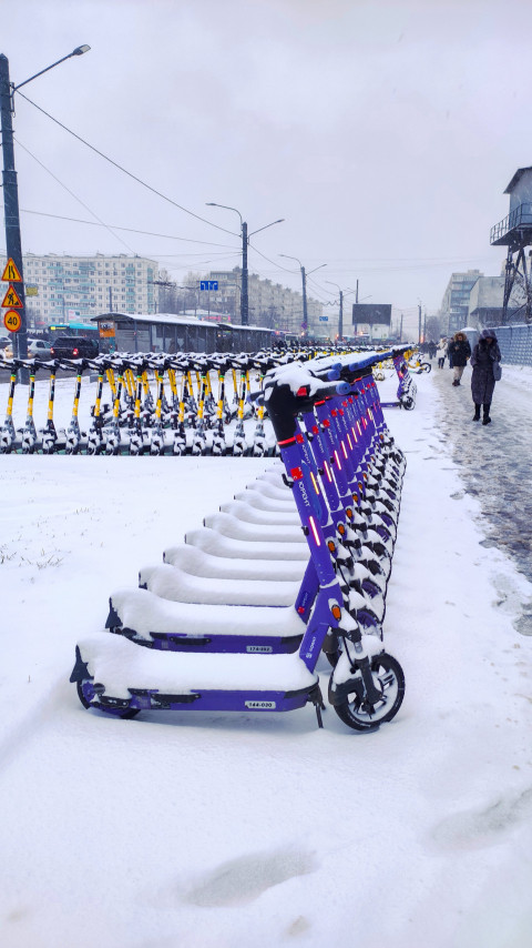 Линия фиолетовых электросамокатов Юрент на фоне городской остановки зимой