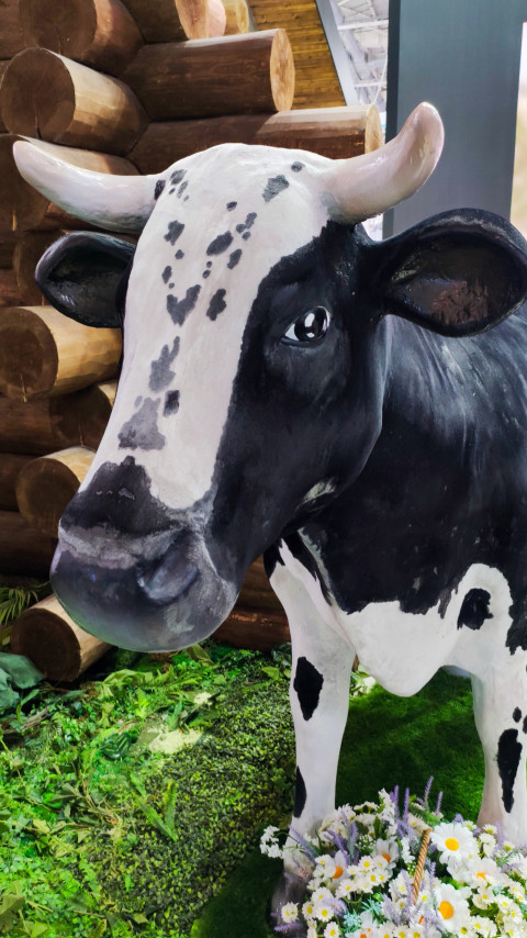 Макет коровы у декоративной деревянной конструкции на выставке