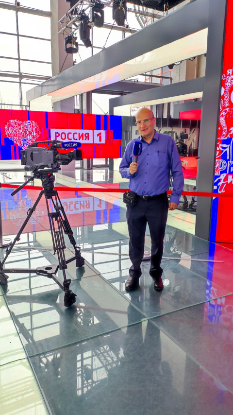 Репортёр с микрофоном «Россия 1» возле телекамеры на выставке