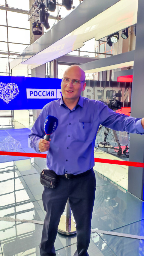 Мужчина с микрофоном «Россия» у стенда телеканала в павильоне №75