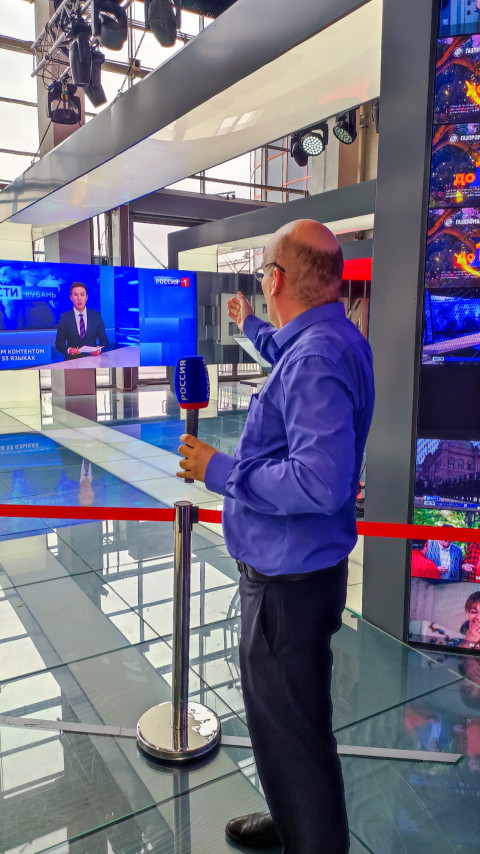 Мужчина с микрофоном перед новостным экраном