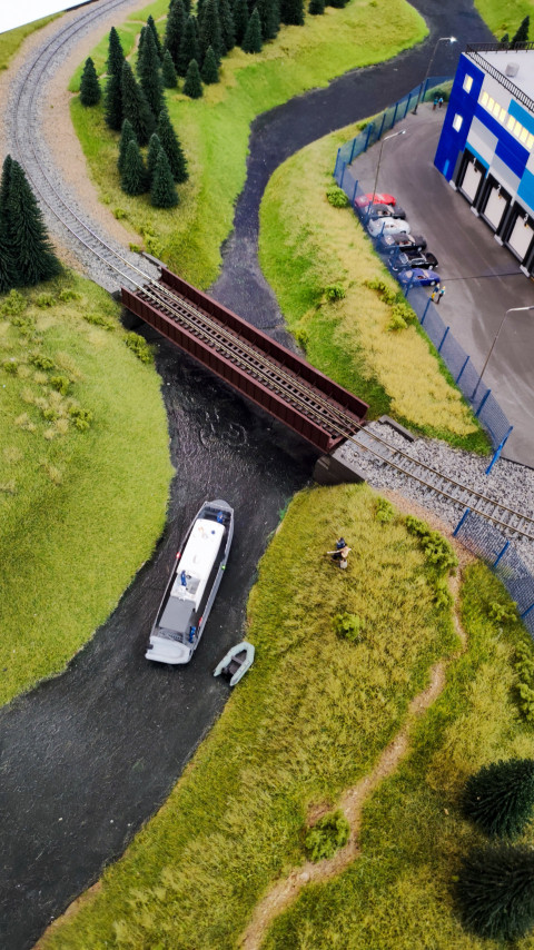 Макет реки под железнодорожным мостом с моторной лодкой