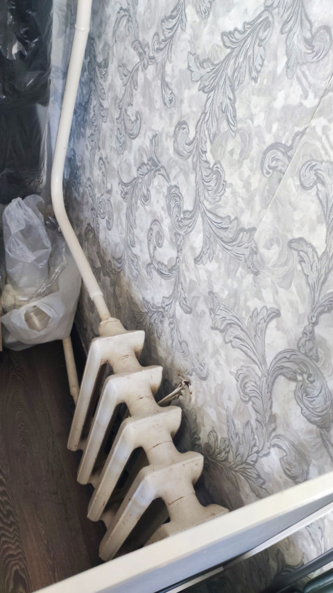 Чугунный радиатор отопления возле стены с узорчатыми обоями