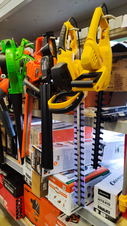 Электрические кусторезы разных брендов на стеллаже магазина