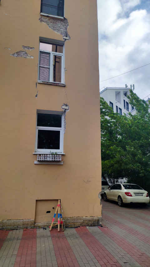 Торцевая стена жилого дома с повреждениями штукатурки и трещинами вокруг окон