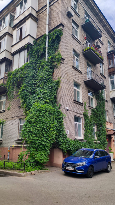 Угловой фасад кирпичного жилого дома с балконами и плющом обыкновенным