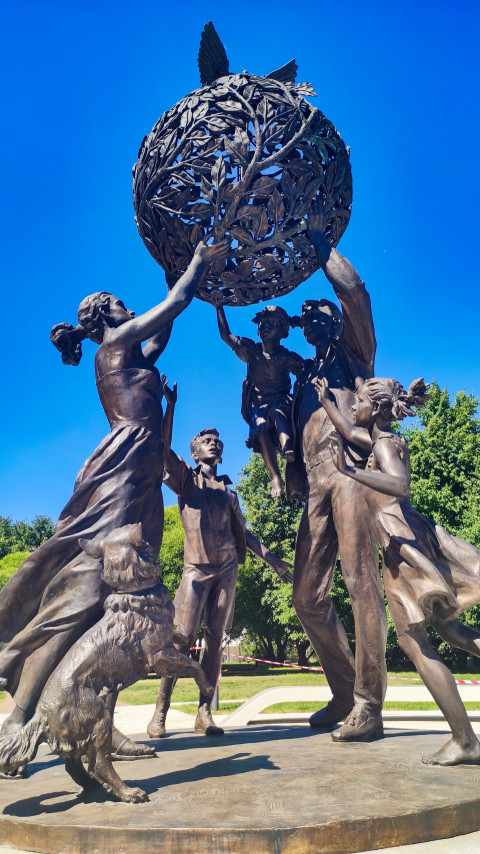 Ракурс снизу на «Семья — залог мира»: фигуры семьи и собака поднимают земной шар с голубями