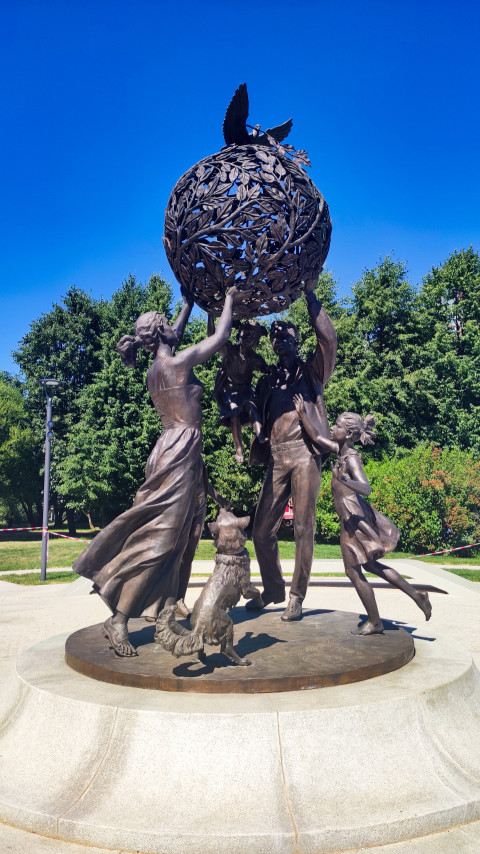 Боковой ракурс монумента «Семья — залог мира» с земным шаром и голубями среди деревьев парка