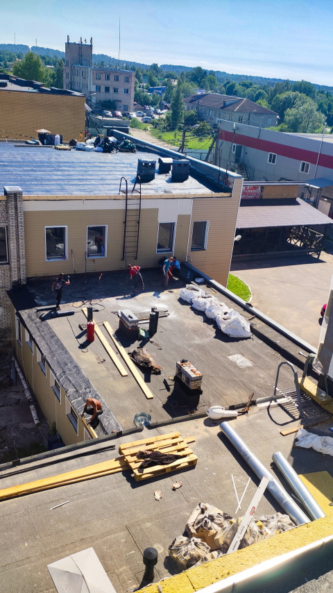 Рабочие выполняют ремонт плоской кровли с рулонной гидроизоляцией на здании