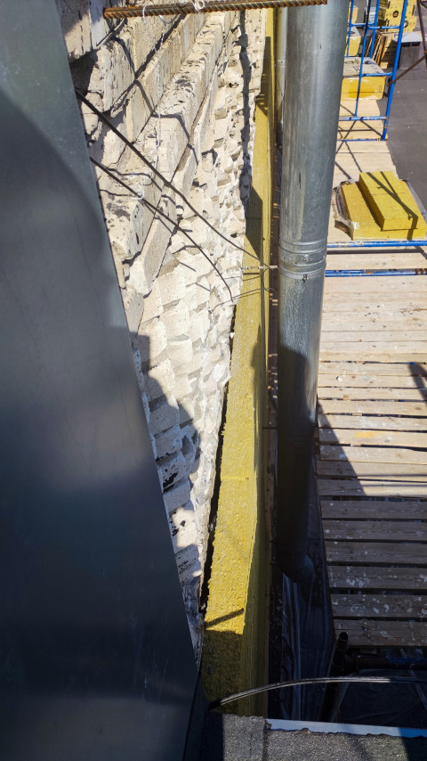 Водосточная труба и утеплитель у стены на настиле строительных лесов