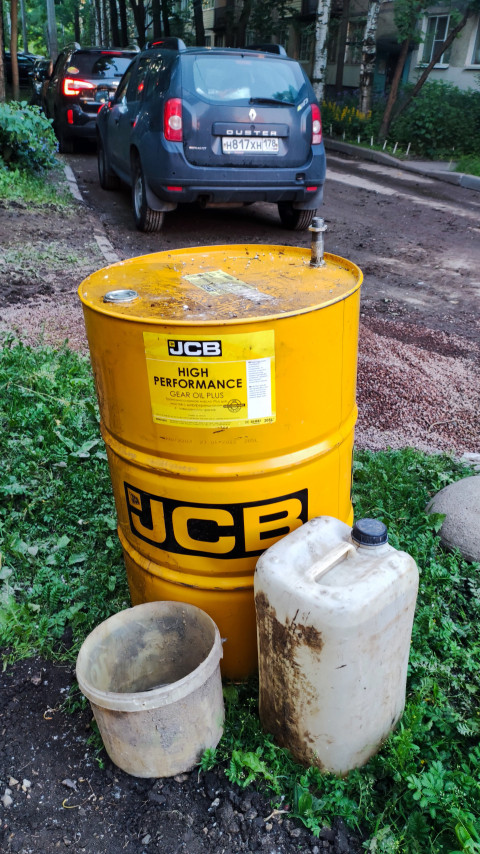Жёлтая бочка JCB с маслом и канистры у проезда во дворе