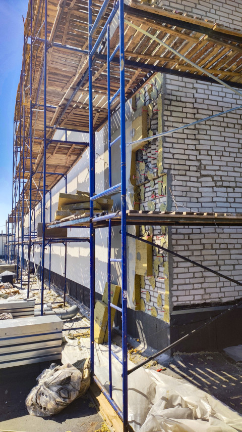 Длинный фасад на строительных лесах с участком вскрытого утепления и повреждённой кладки