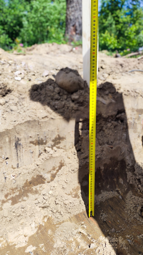 Рулетка в траншее показывает глубину выемки грунта при земляных работах