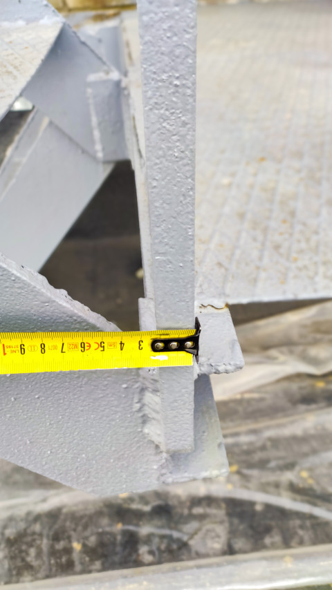 Крюк рулетки фиксирует замер у торца серой металлической конструкции