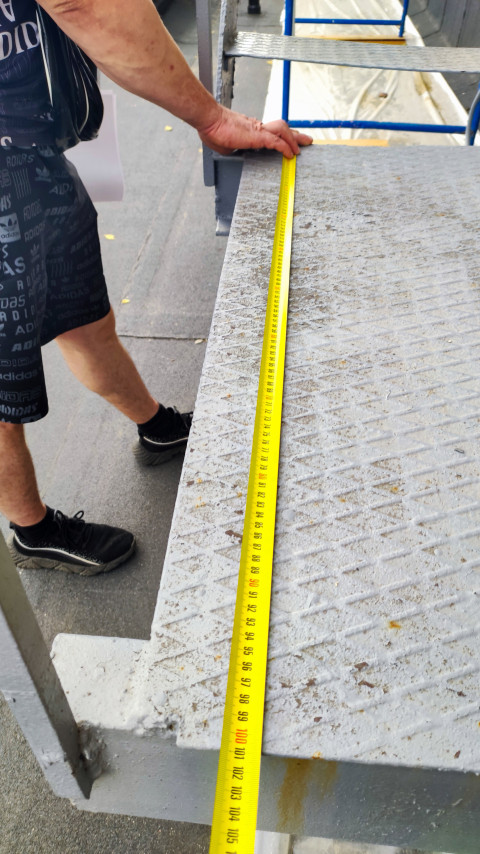 Рулетка натянута вдоль металлической площадки при замерах на строительном объекте