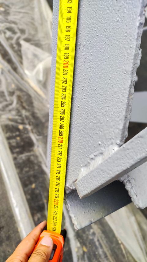 Рулетка измеряет высоту стойки металлической конструкции, видна рука с инструментом