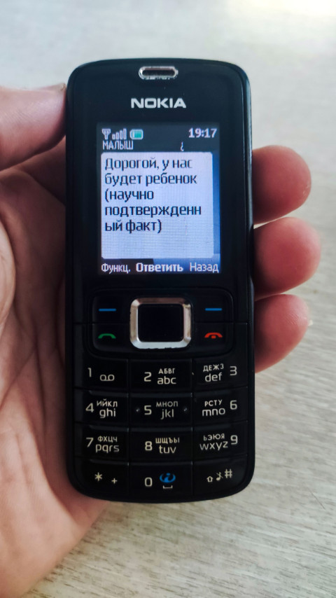 Кнопочный телефон Nokia в руке показывает SMS «Дорогой, у нас будет ребёнок»
