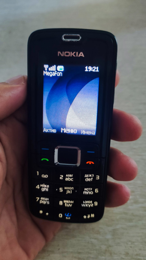 Кнопочный телефон Nokia в руке с экраном ожидания и индикатором сети MegaFon