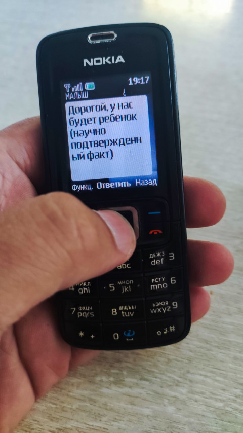 Кнопочный Nokia с открытым SMS о будущем ребёнке снят под углом на светлом фоне