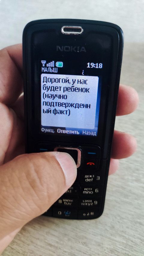 Кнопочный Nokia с SMS о будущем ребёнке в руке на фоне светлой поверхности