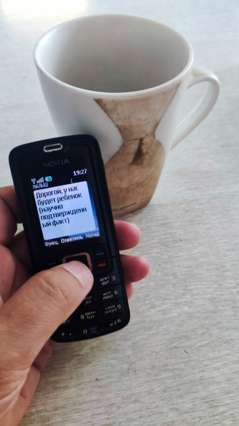 Телефон Nokia с открытым SMS рядом с керамической кружкой на столе