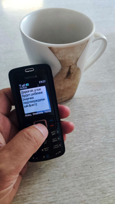 Кнопочный телефон Nokia в руке с SMS о беременности на фоне кружки на столе