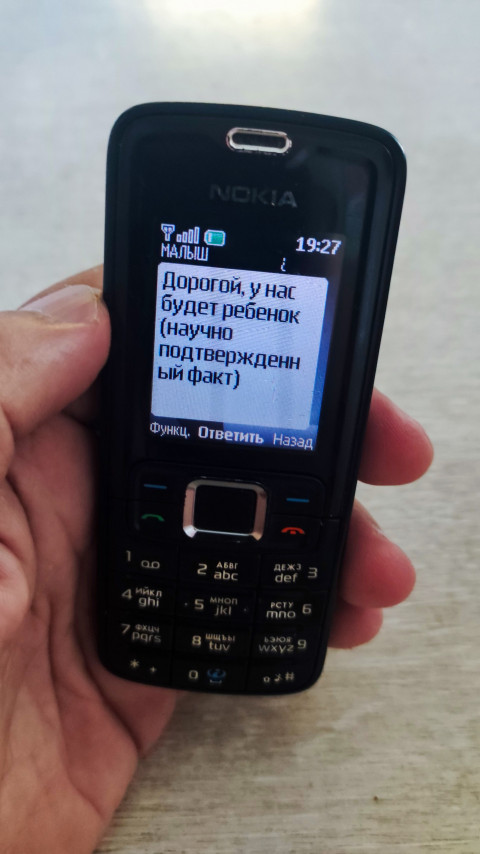 Экран кнопочного телефона Nokia с SMS о будущем ребенке в руке человека