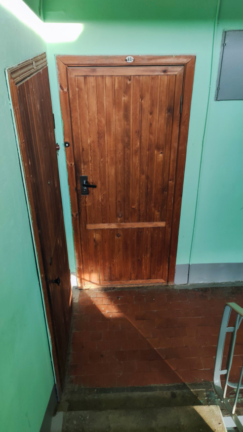 Деревянная дверь с номером 83 на лестничной площадке подъезда при дневном свете