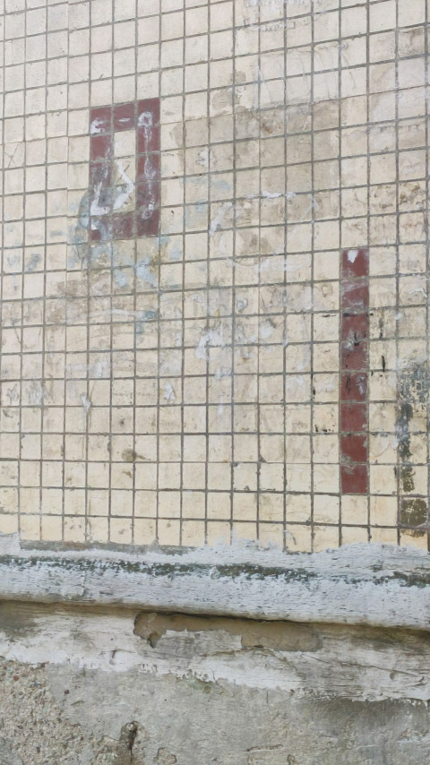 Старая плиточная облицовка стены с потёртостями и остатками красной разметки крупным планом