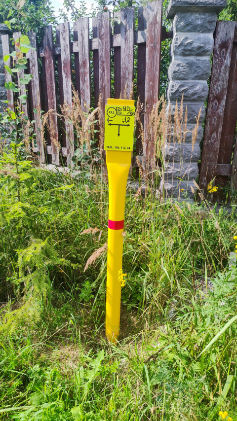 Жёлтый сигнальный столбик газопровода у деревянного забора и каменного столба