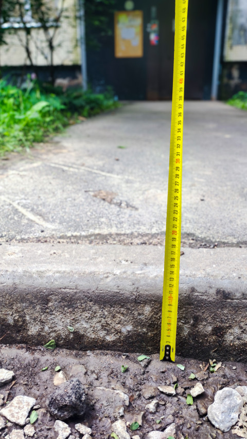 Рулетка у бордюра возле входа в подъезд на фоне двери с информационным стендом