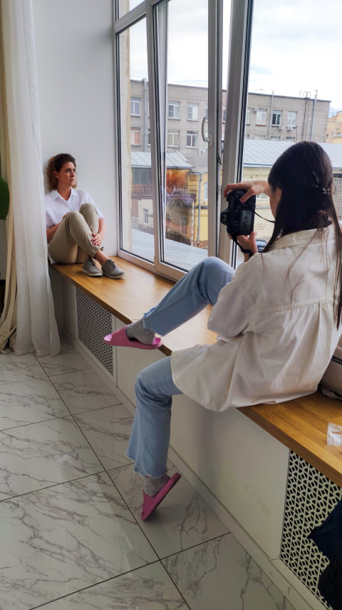 Женщина сидит на подоконнике у окна, фотограф снимает крупный план